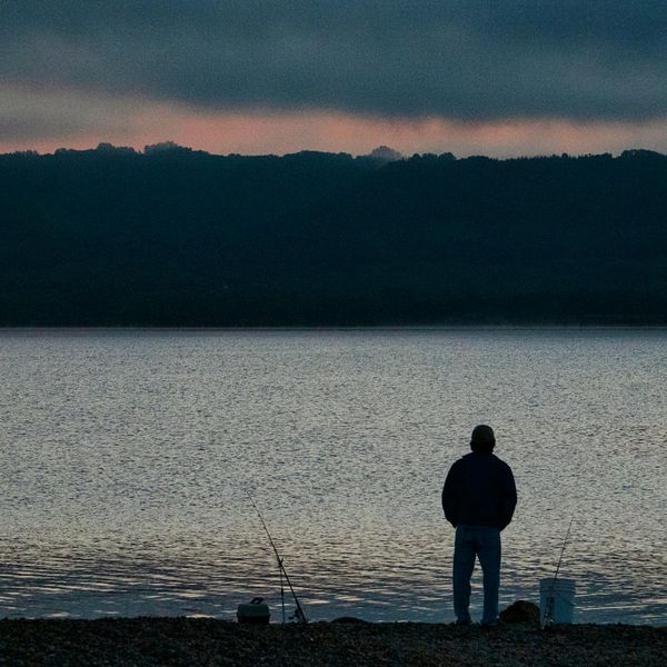 Person meditating peacefully outdoors near a calm lake at sunrise.